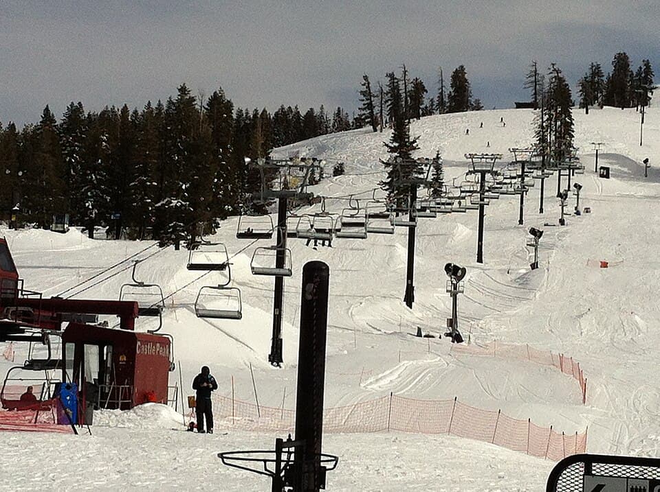 Boreal's base-area slopes with two chairlifts running up the hill, a terrain-park fence line and skiers, on an overcast March day.