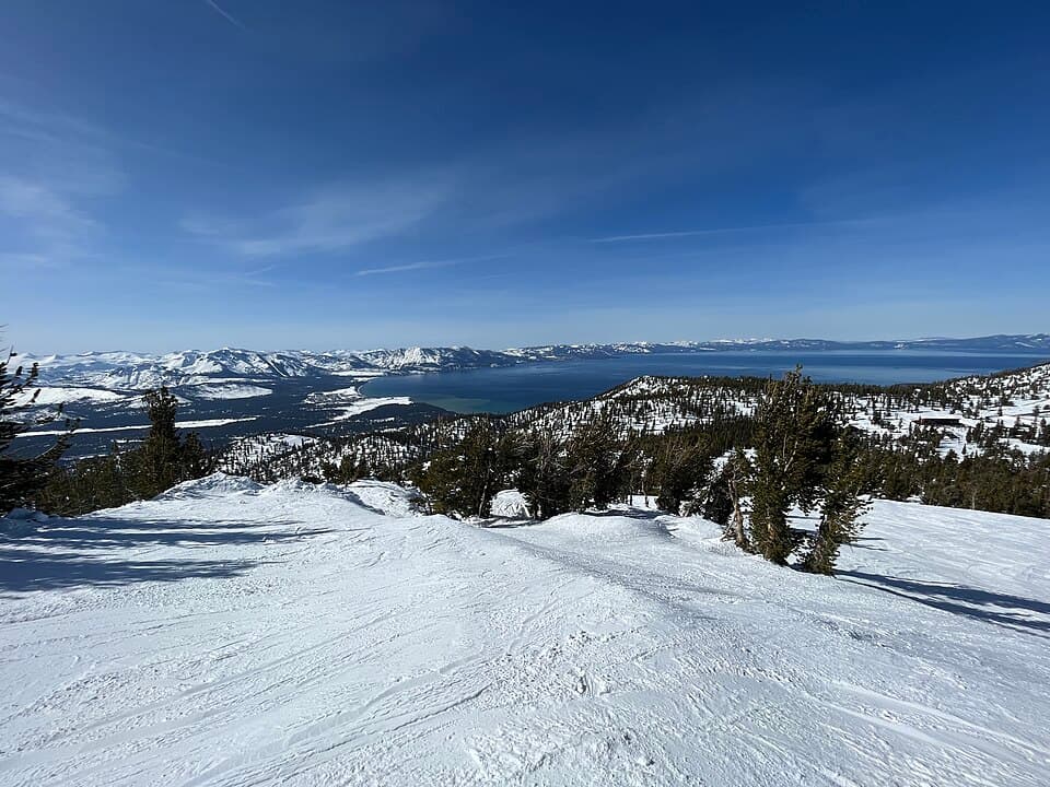Looking out from Heavenly's upper slopes across the full width of a deep-blue Lake Tahoe, snow-covered peaks ringing the far shore.
