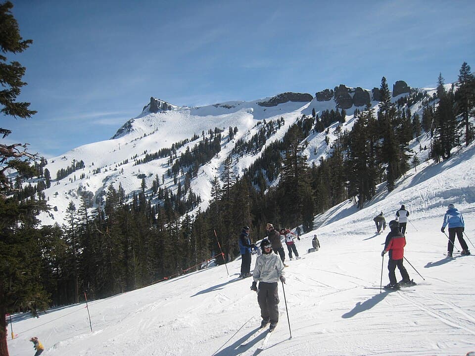 Skiers spread across a sunlit Kirkwood run with the resort's signature jagged volcanic cliff band rising behind.