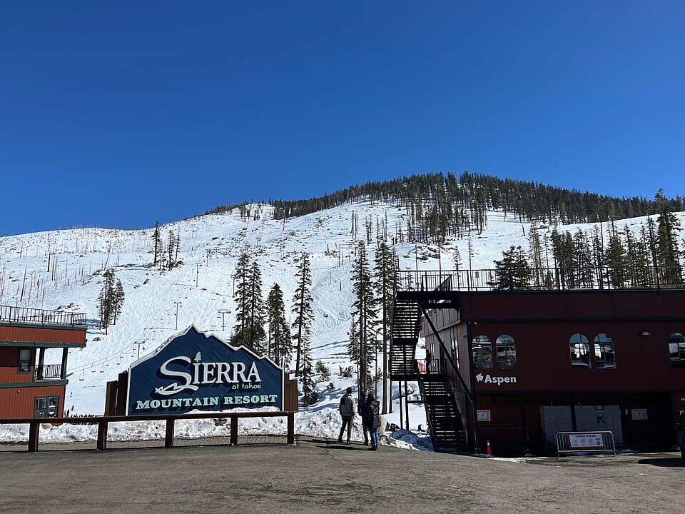 Sierra-at-Tahoe's base area on a clear March day - the 'SIERRA at Tahoe Mountain Resort' entrance sign and the Aspen building in the foreground, with the ski hill rising behind.