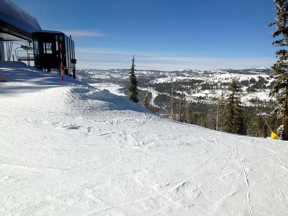 Groomed snow at a Sugar Bowl summit lift station under deep blue sky, looking out over miles of white Sierra ridges toward Donner Pass.